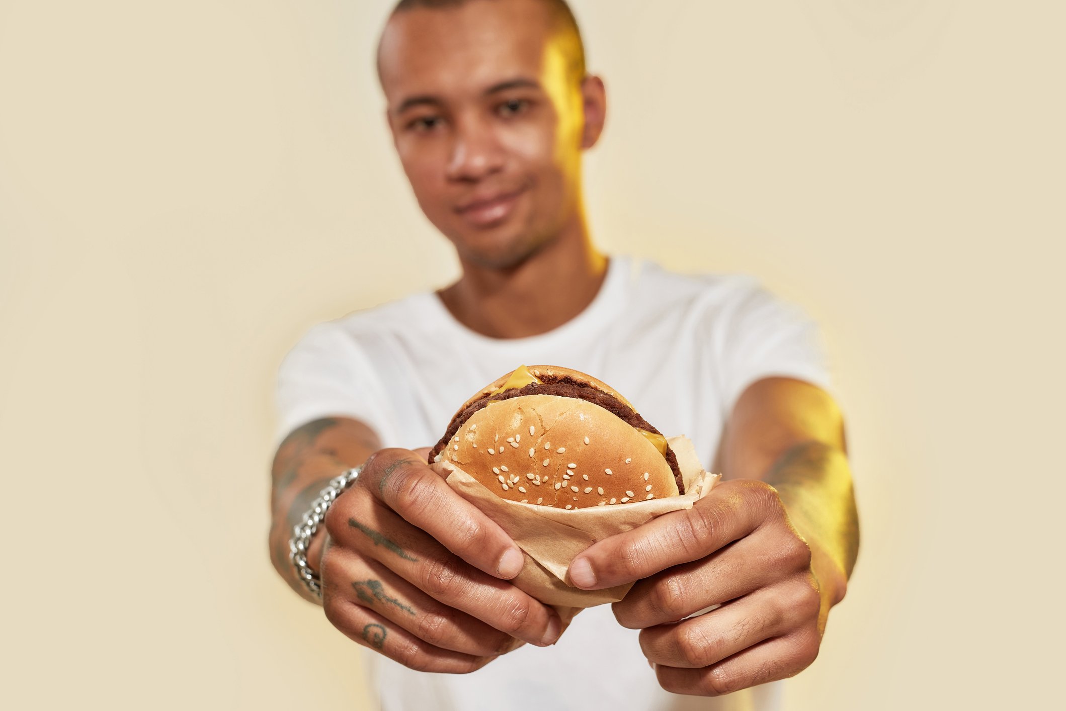 Person thrusting a hamburger at the camera.