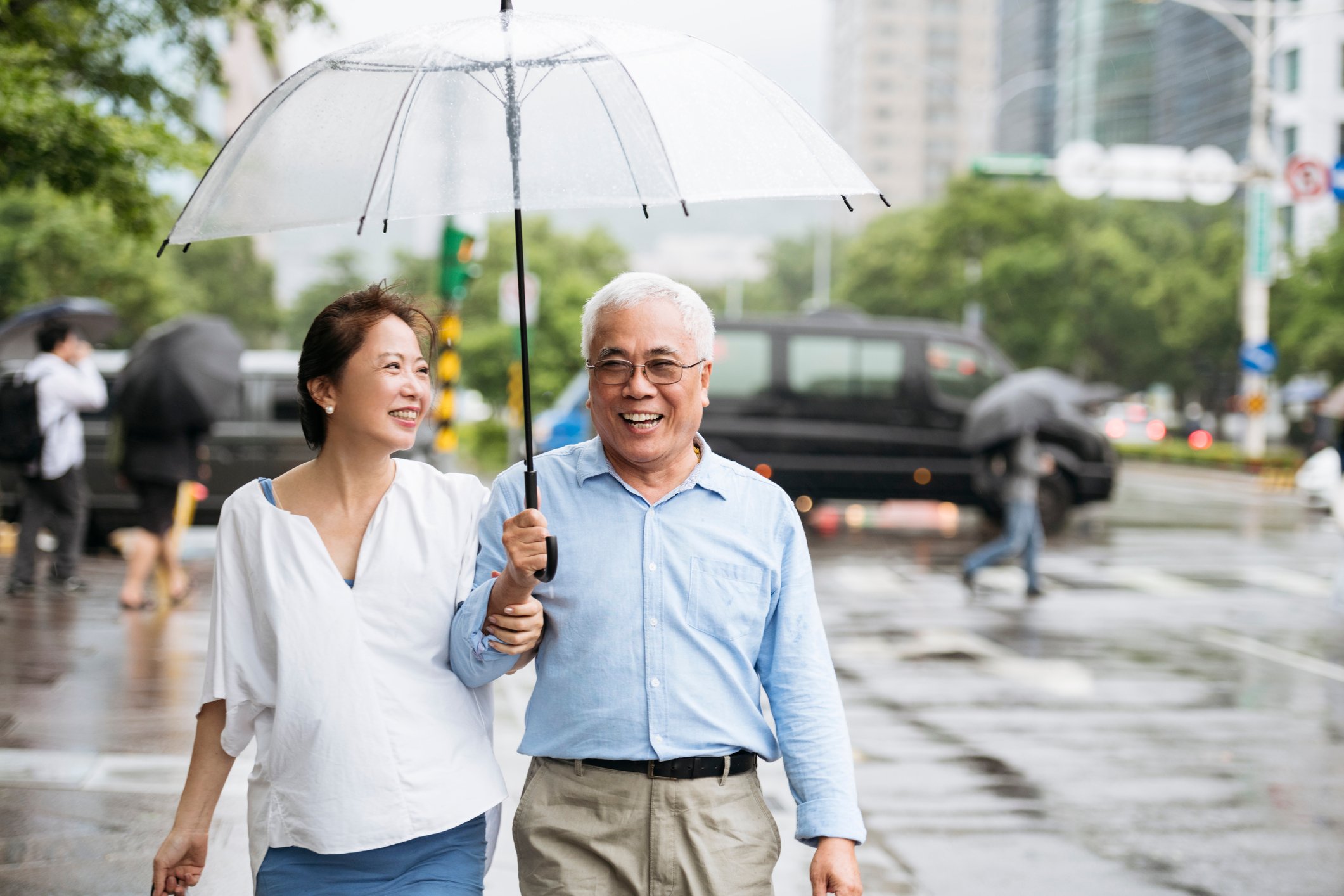 A smiling couple is walking, holding an open umbrella.