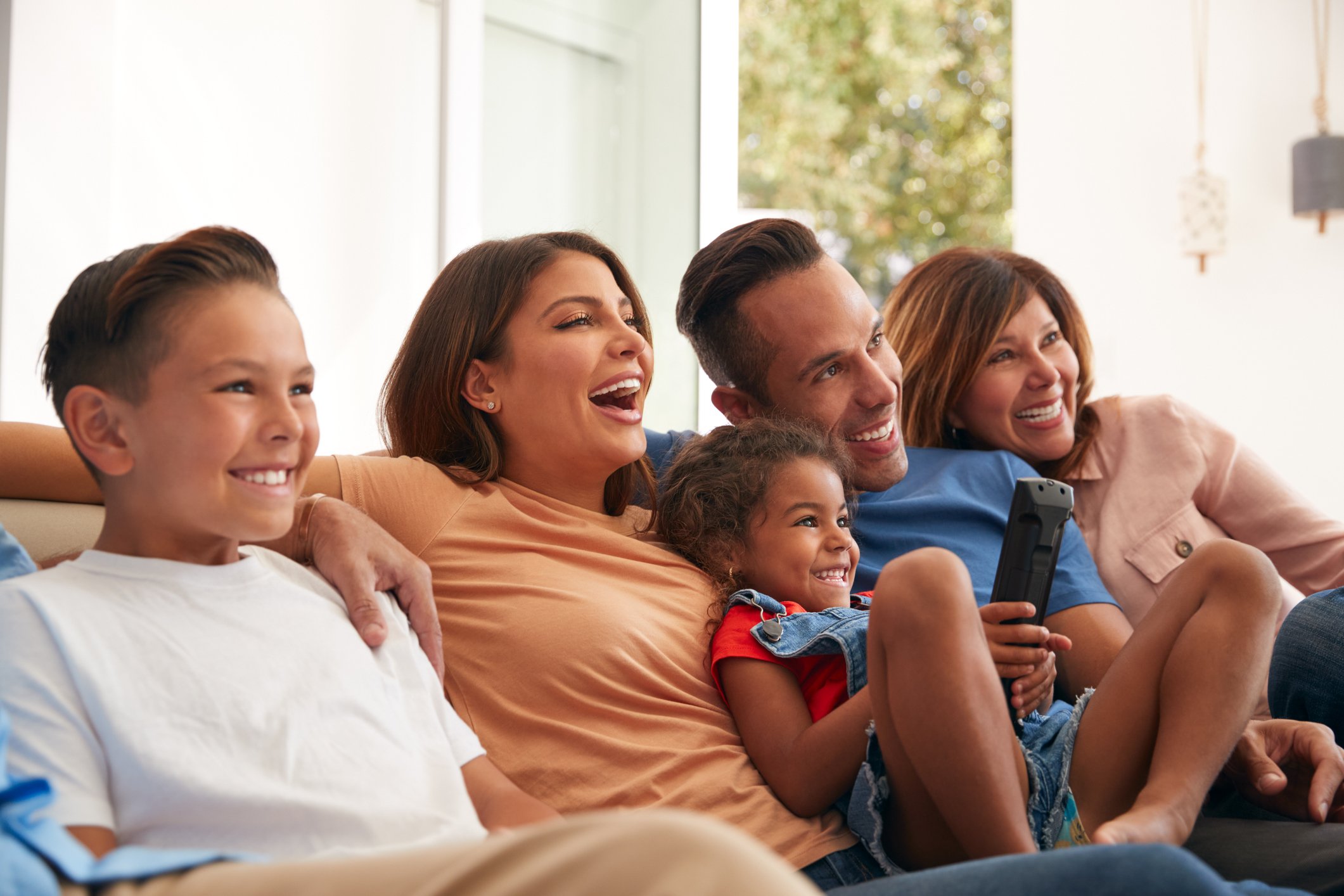 A family sits on the couch and smiles as they watch television.