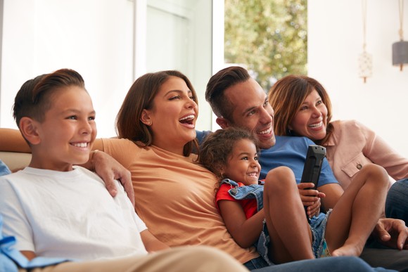 A family sits on the couch and smiles as they watch television.