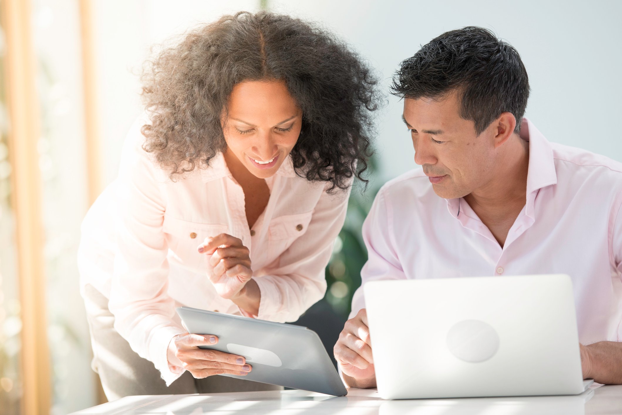 A smiling person showing something on a touchscreen tablet to another person.