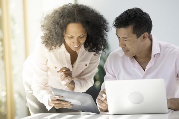 A smiling person showing something on a touchscreen tablet to another person.