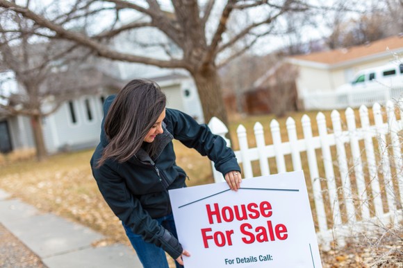 A person is hanging a for sale sign on a house. 