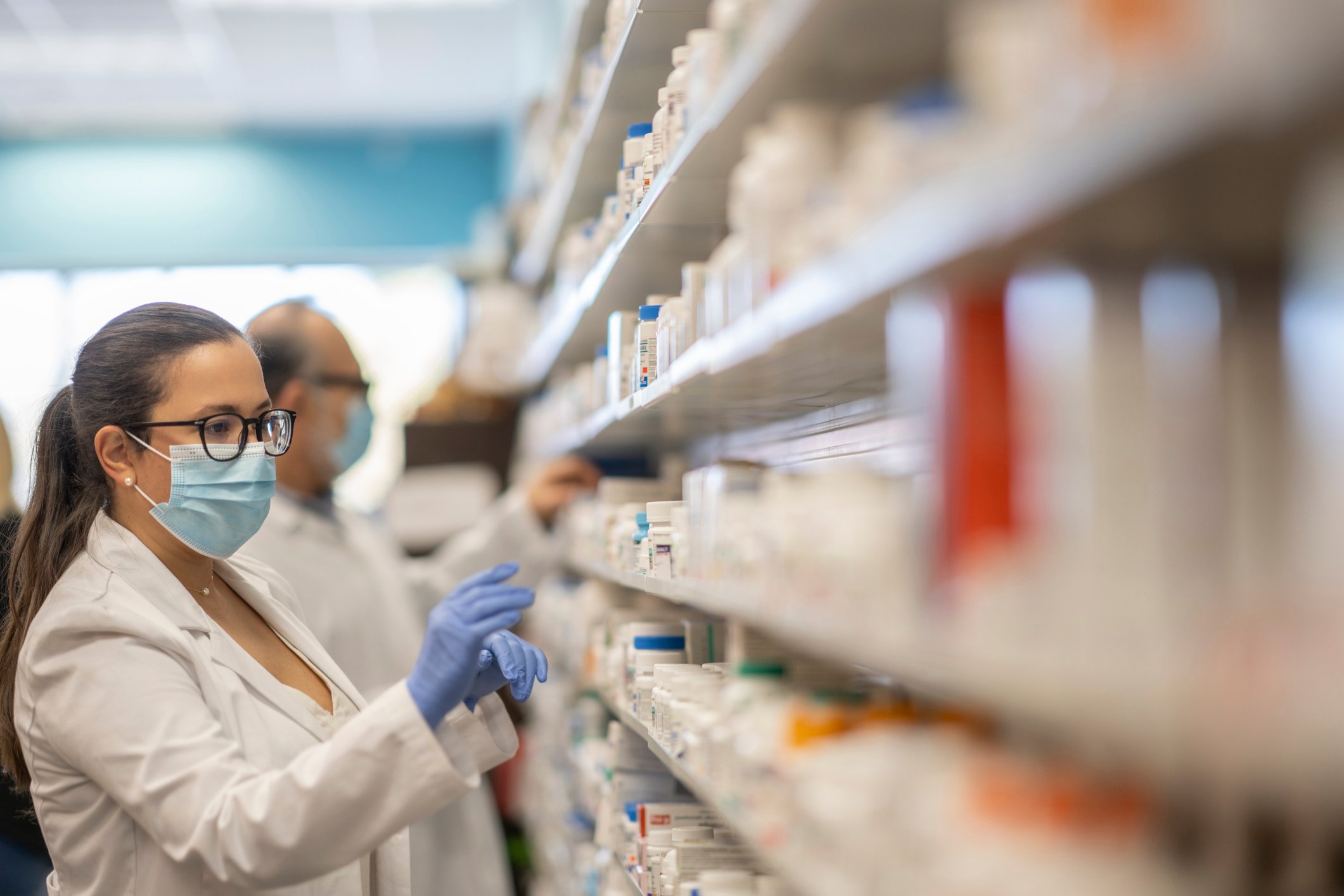 A pharmacist chooses a medicine from a shelf.