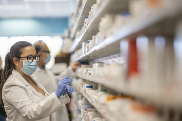 A pharmacist chooses a medicine from a shelf.