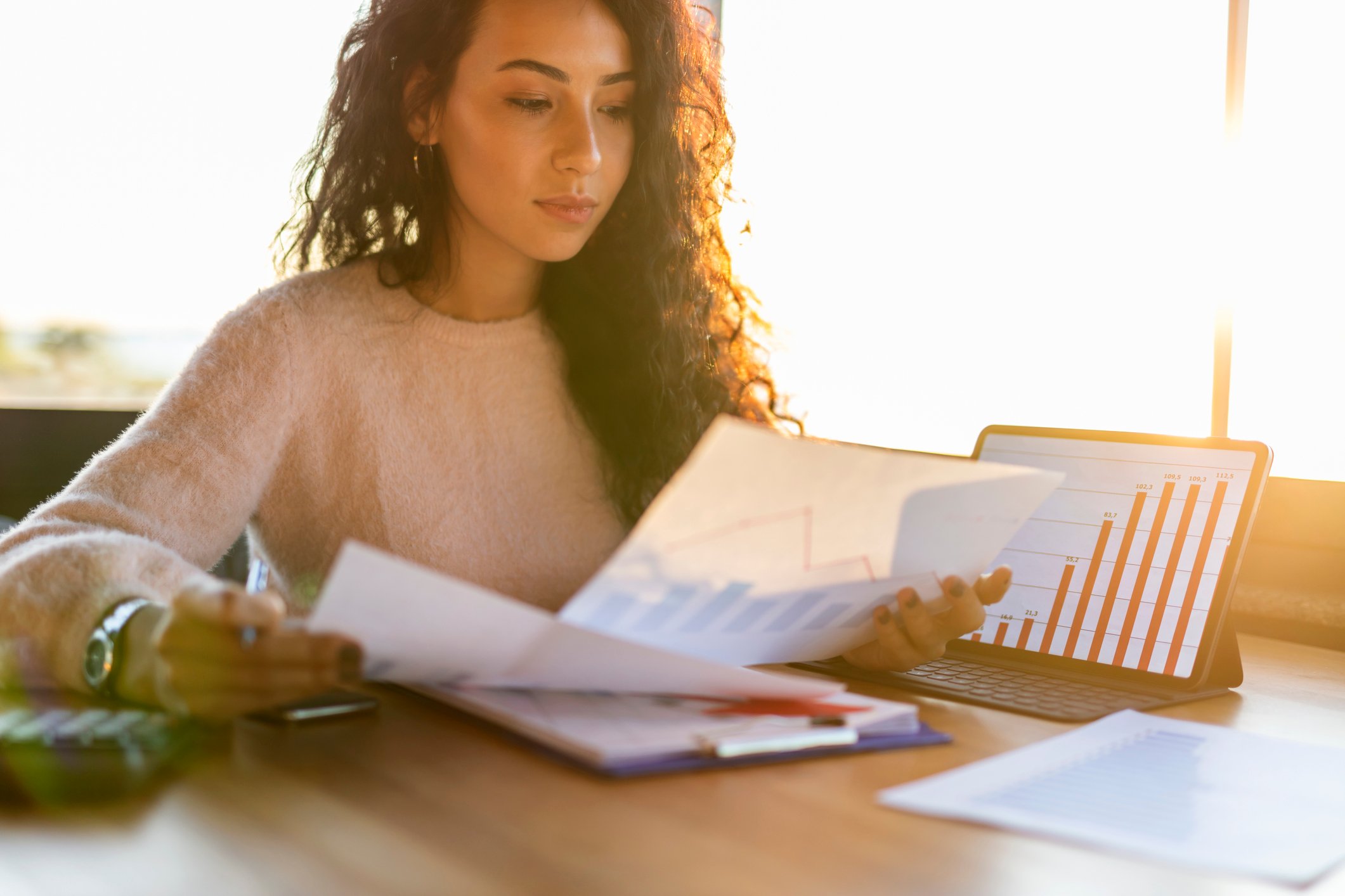 Person analyzing price charts using her digital tablet and paper documents.