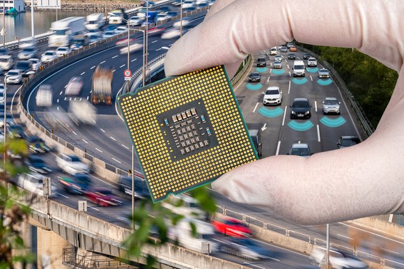 A hand holding a computer chip with a background of freeway traffic.