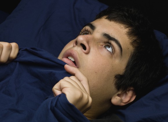 Wide-eyed person in bed, holding the comforter tight and staring at the ceiling.