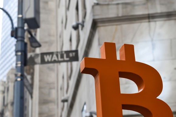 A bitcoin logo sitting in front of the Wall Street sign in New York.