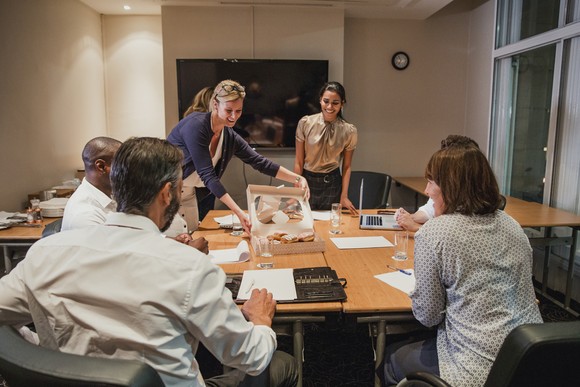 Person opening box of donuts at a conference table.