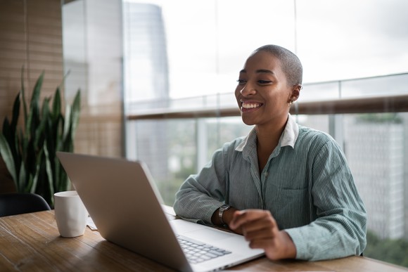 A person smiling and working on a laptop computer.