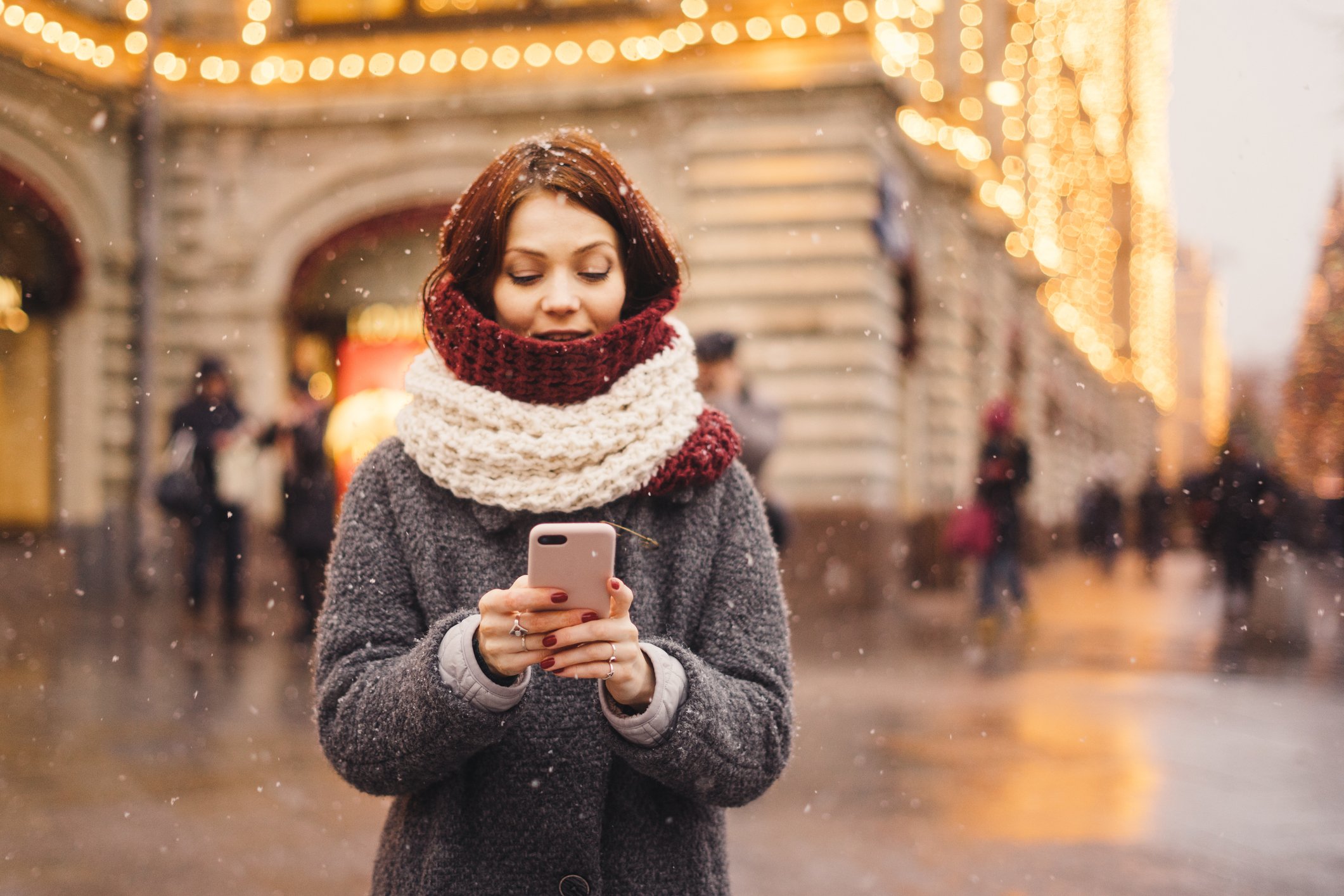 A person in winter clothing uses a smartphone outside.