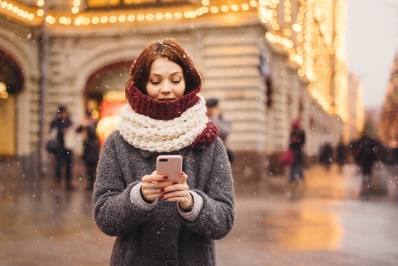 A person in winter clothing uses a smartphone outside.