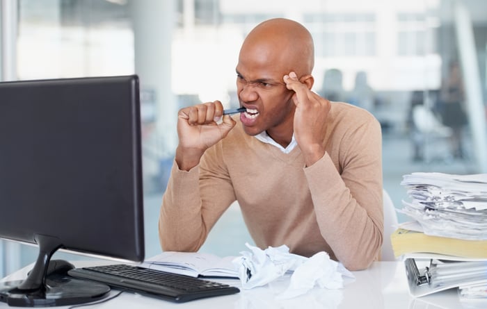 A frustrated investor staring at a monitor while biting down on a pen.