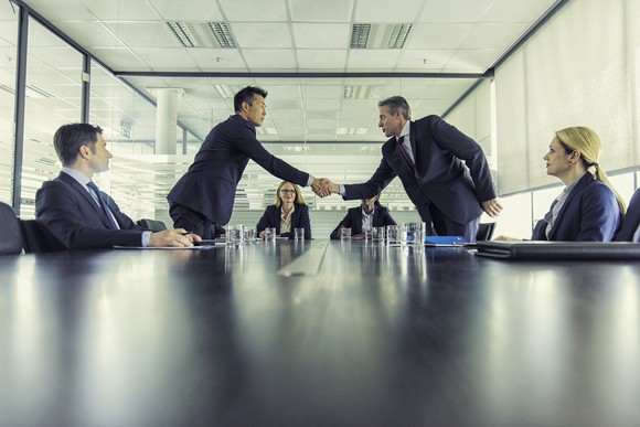 People are shaking hands in a boardroom. 