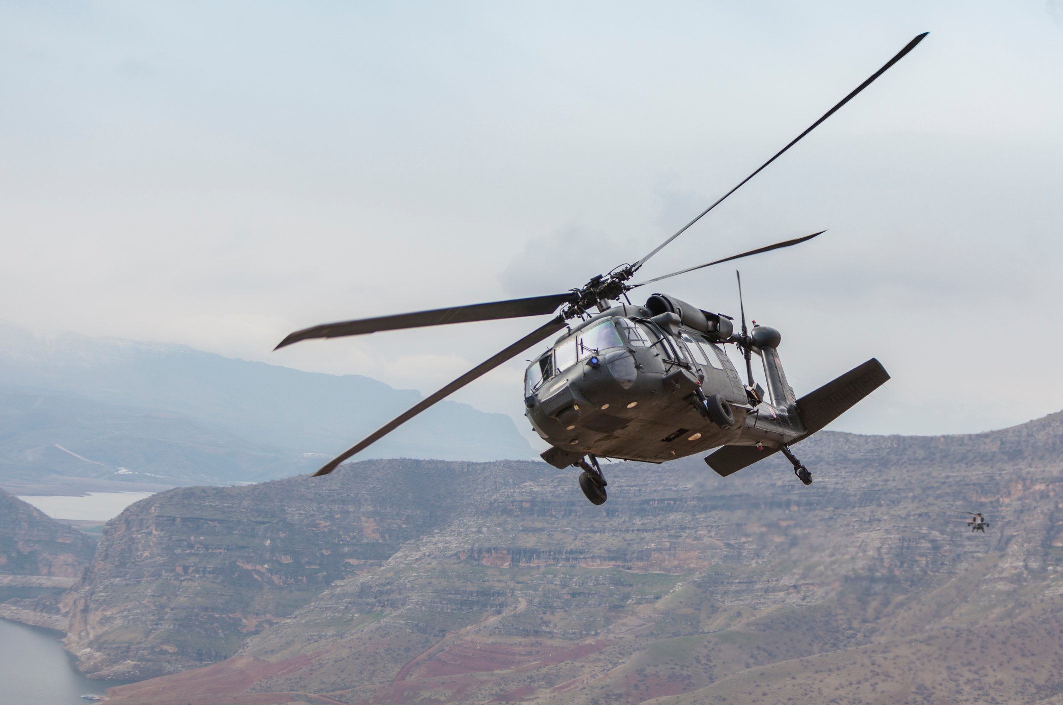 A UH-60 Black Hawk helicopter flying over a river valley. 