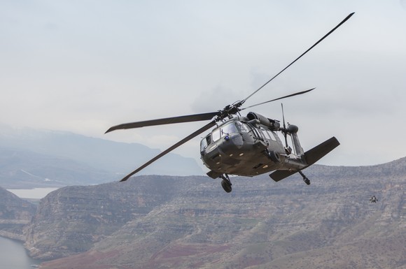 A UH-60 Black Hawk helicopter flying over a river valley. 