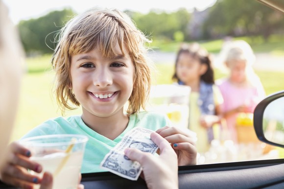 A child sells a cup of lemonade to a driver.