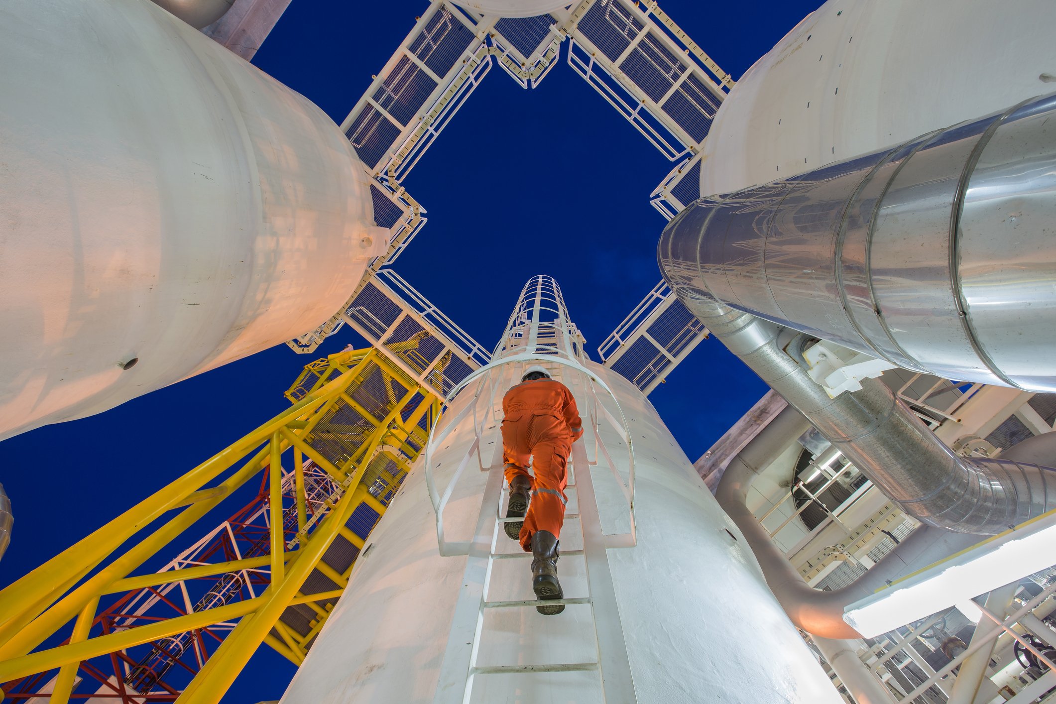 Worker in orange suit climbing ladder at natural gas facility.