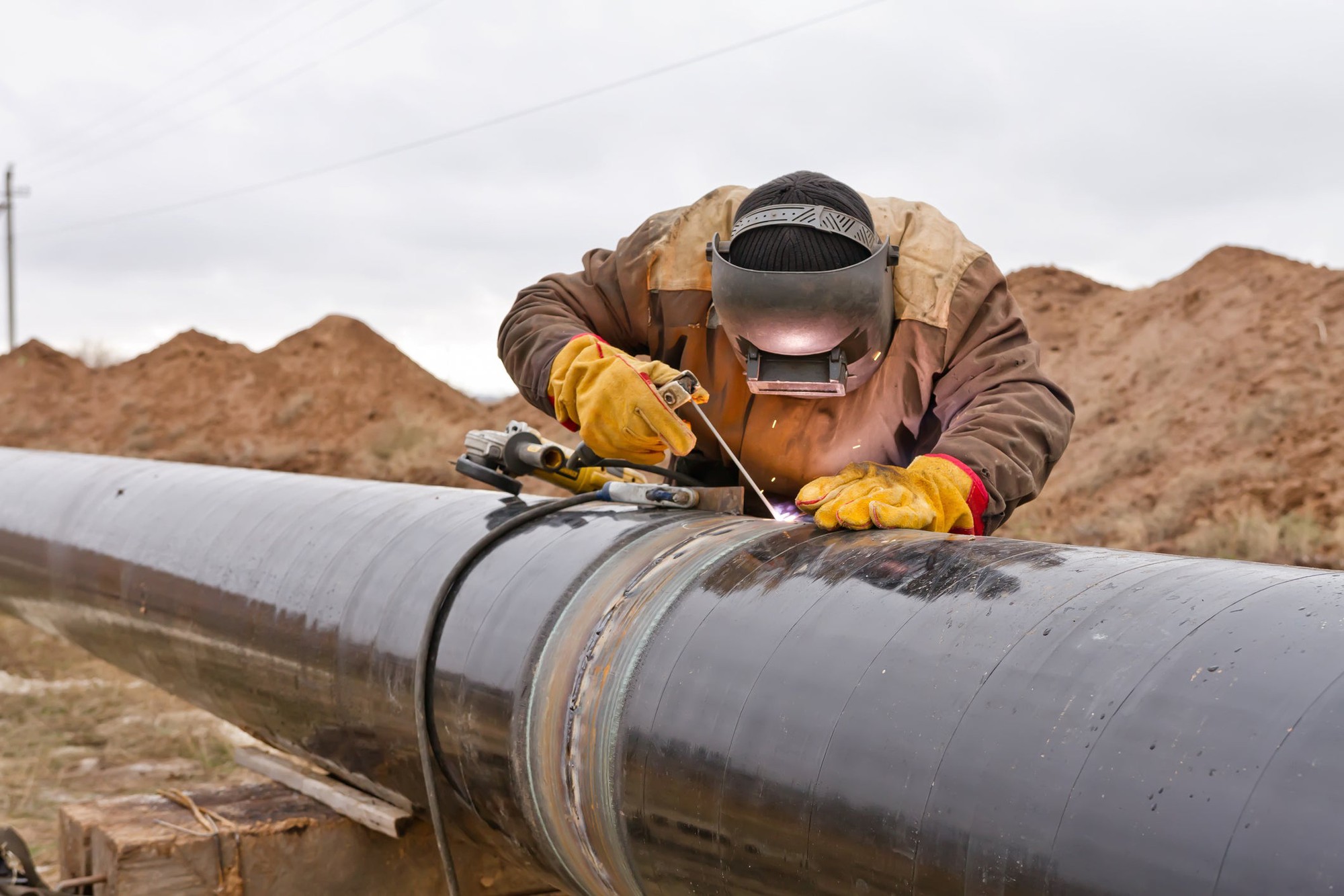 A man welding an above-ground pipeline. 