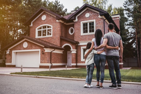 Two adults and child stand in front of house.
