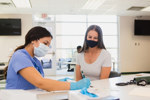 A nurse writes on a piece of paper while sitting at a table with a patient.