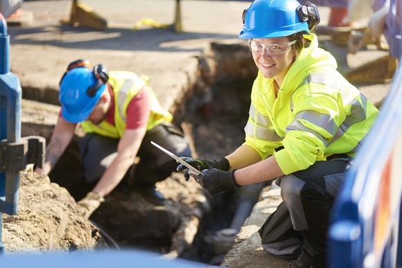 Workers laboring in, and next to, an open trench.