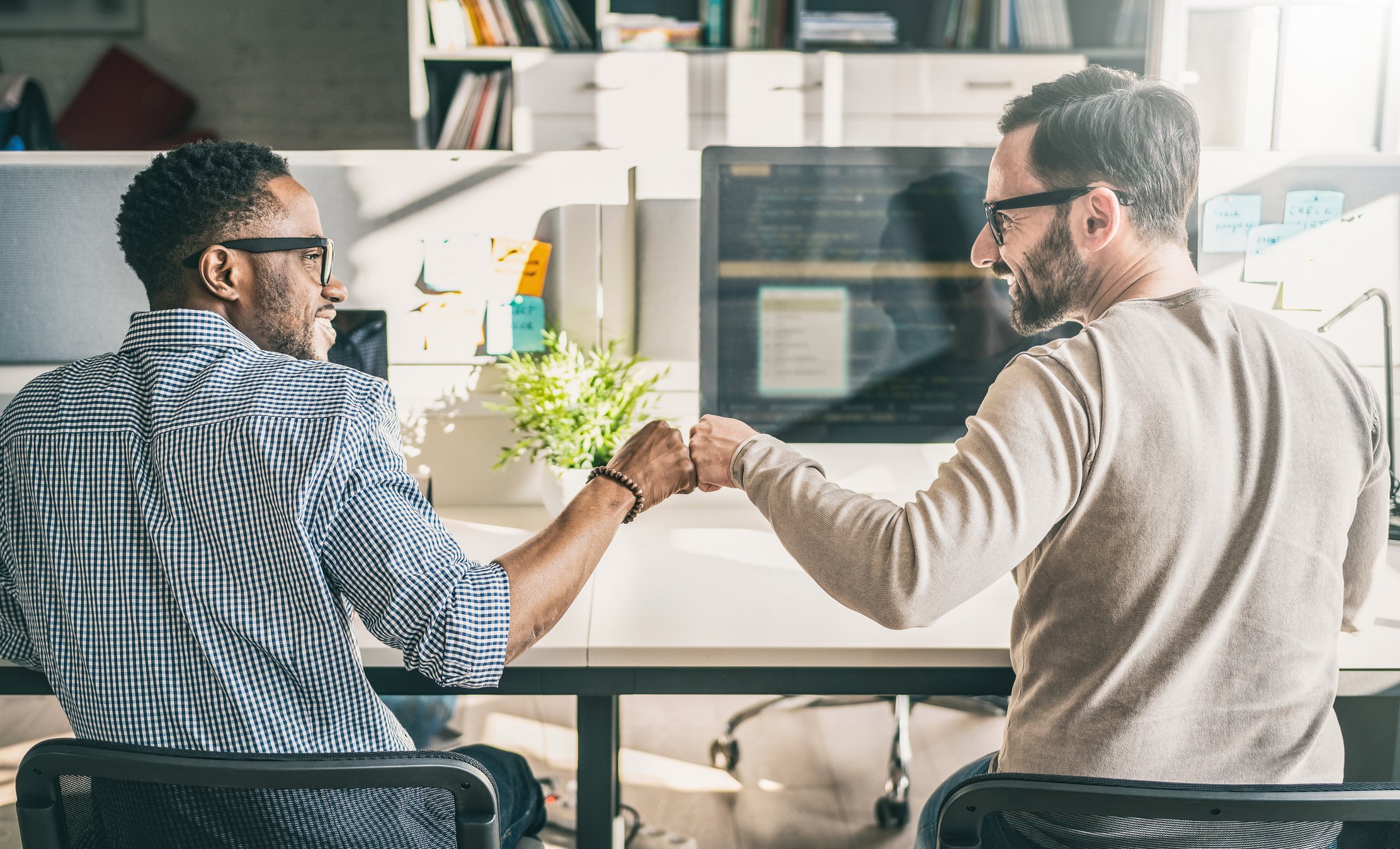 Two colleagues smile and bump fists.