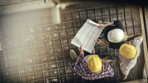 Three construction workers inspecting plans while standing on rebar.