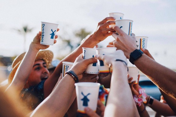 Several arms reach Dutch Bros coffee cups up in celebration.