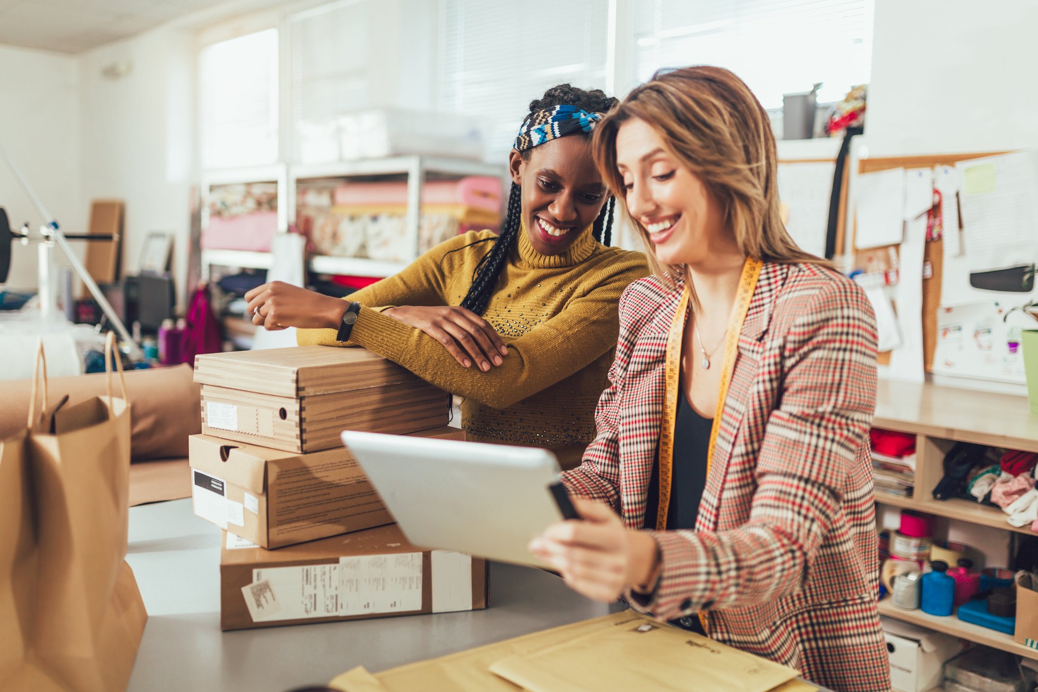 People are smiling as they look at a tablet computer near a stack of cardboard boxes. 