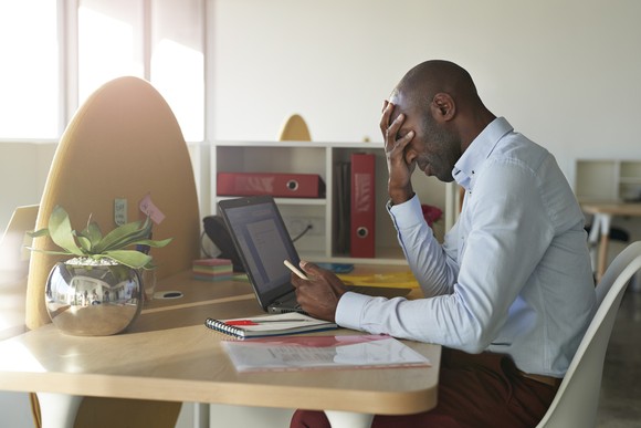 A person sits at a desk holding their head in their hands.