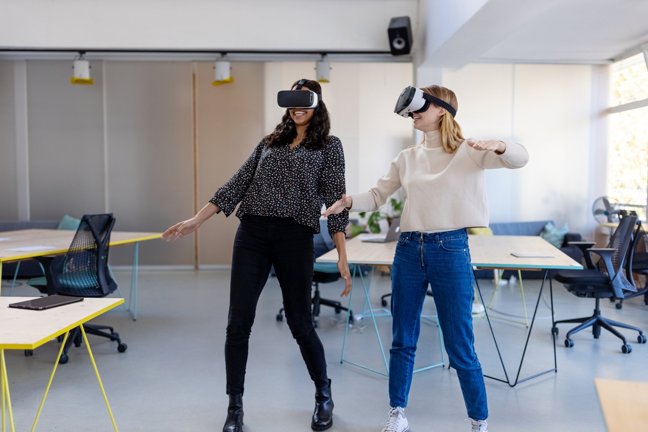 Two office workers stand in a meeting room while wearing VR headsets.