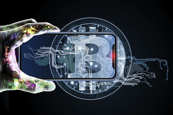 Person holding phone on top of a Bitcoin symbol.