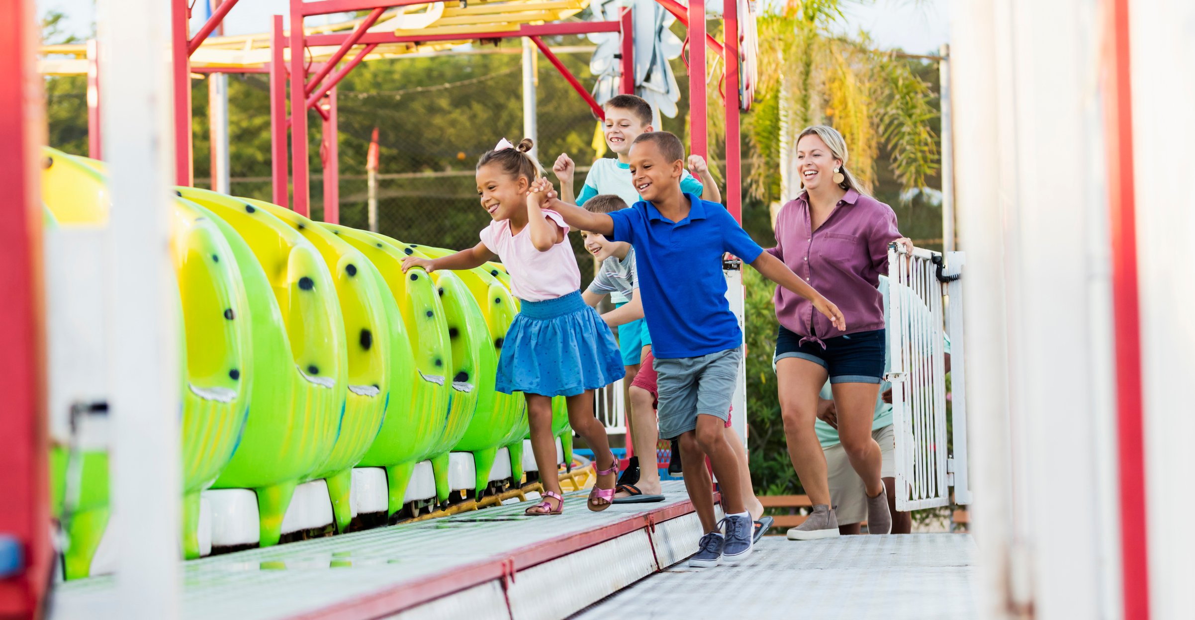 Children entering a theme park thrill ride under an adult's watchful eye.
