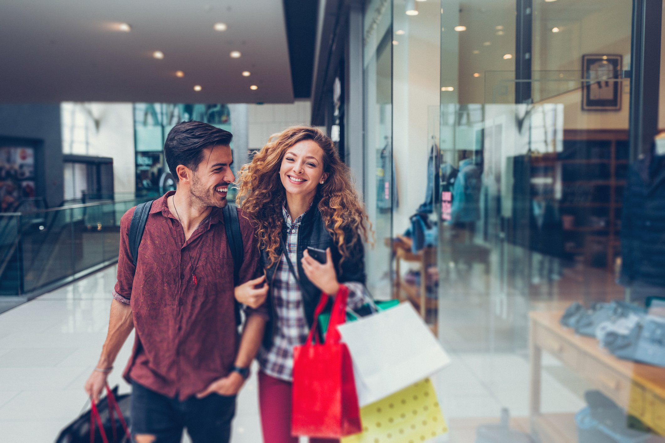 Smiling young couple toting merchandise bags in a shopping center.