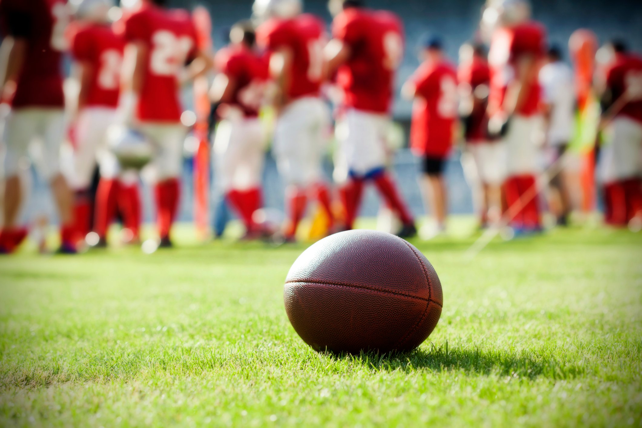 A football on a field with players standing in the background.