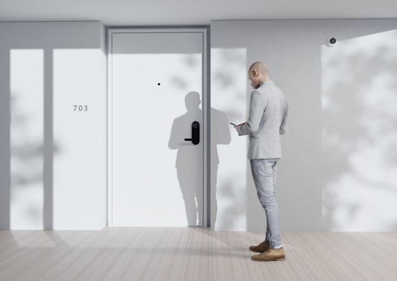 A man approaches an apartment door while looking at his smartphone. The person is using the smartphone to unlock a Latch-equipped door 