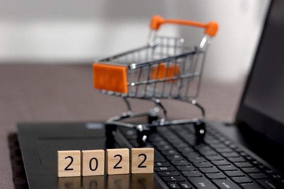 A mini shopping cart and the number 2022 written in blocks on a laptop computer illustrating online shopping trends today.