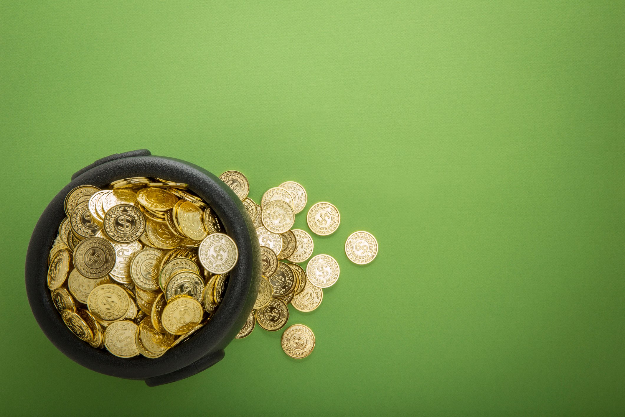 Pot of gold with gold coins on green surface.