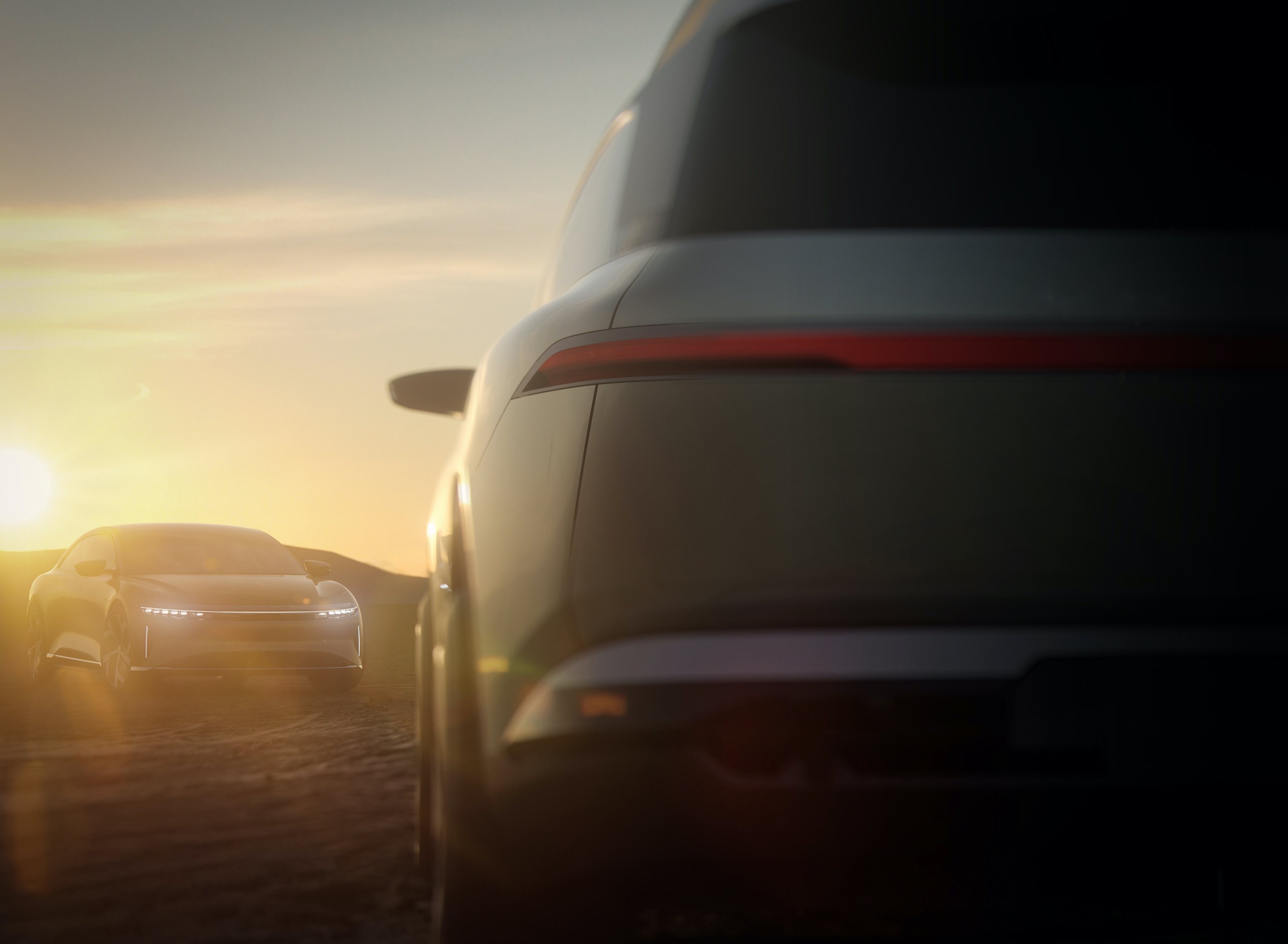 The back of a Lucid Gravity concept car and a Lucid Air electric sedan in the background at dawn.