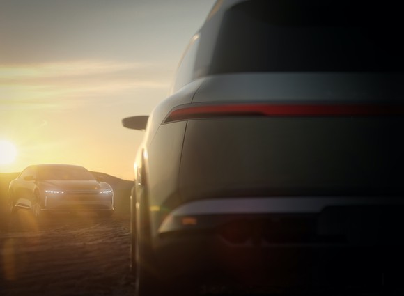 The back of a Lucid Gravity concept car and a Lucid Air electric sedan in the background at dawn.