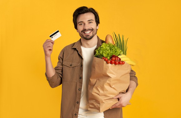 Person holding payment card and grocery bag.