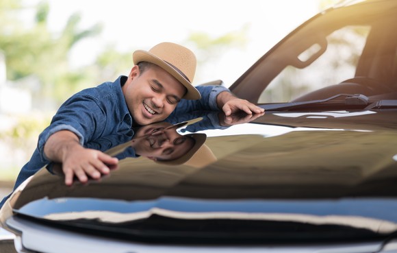 A smiling person hugs the hood of a truck.