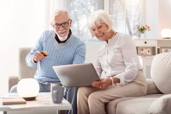 Elderly couple working with laptop in living room.