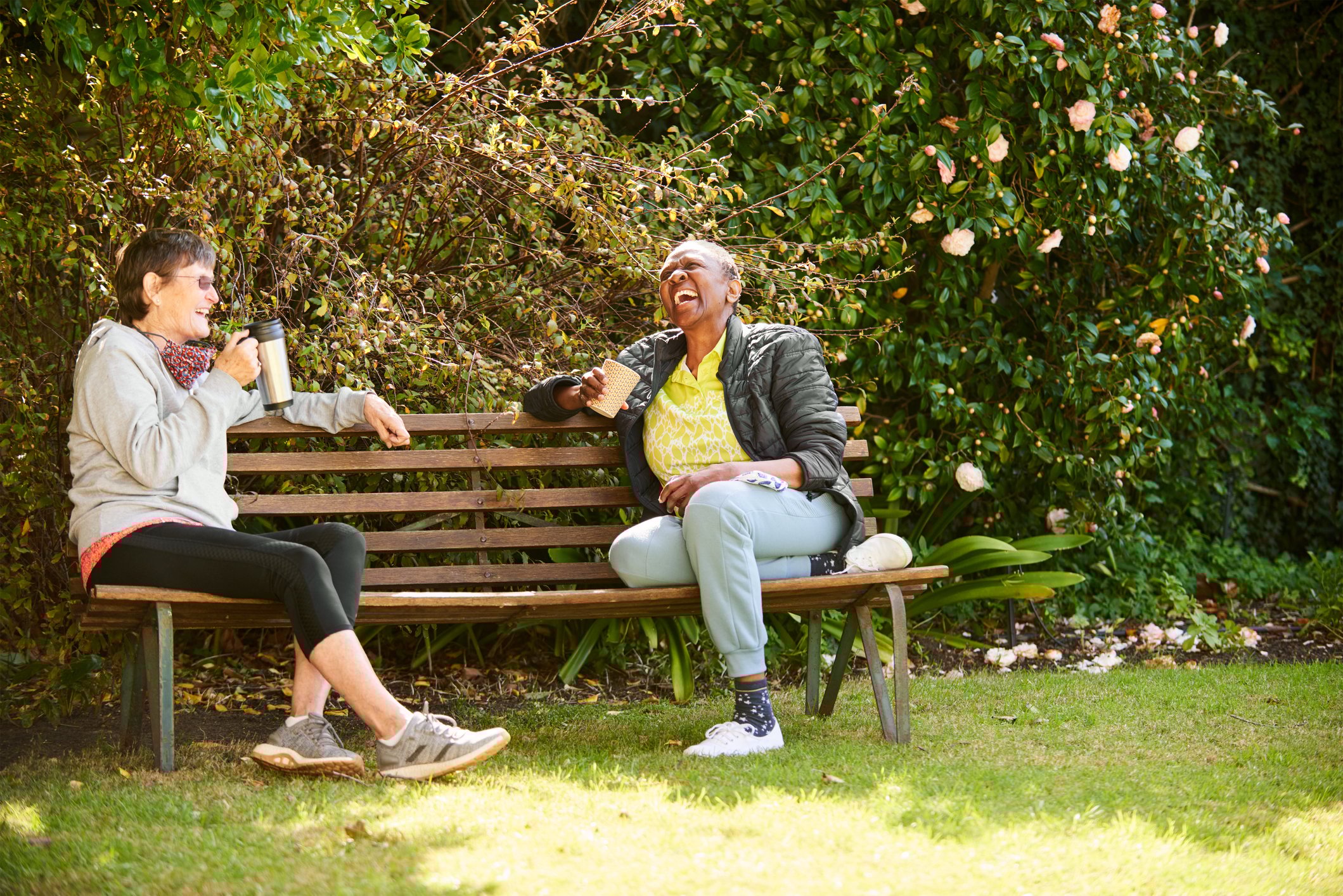 Two older people sitting on bench and laughing.