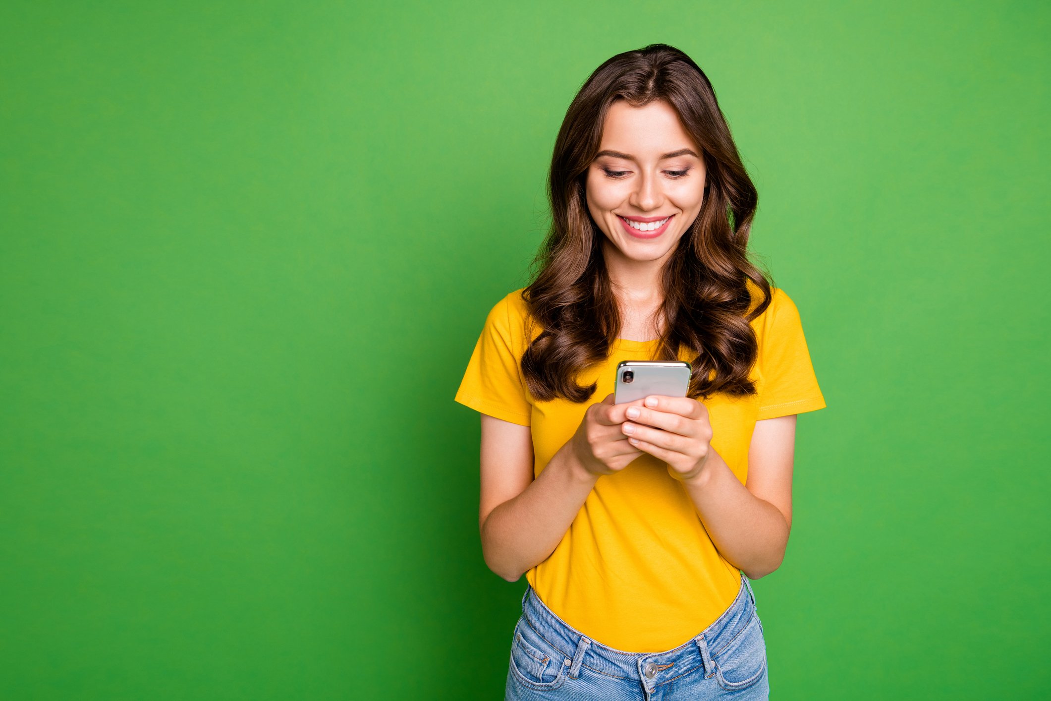 A woman using a phone in front of a green background.