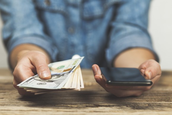 A person holding some cash and a phone. 