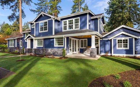 Exterior of large deep blue-shingled house surrounded by ample greenery.