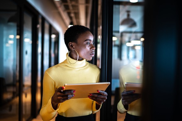 A person checks a tablet while standing in a hallway.